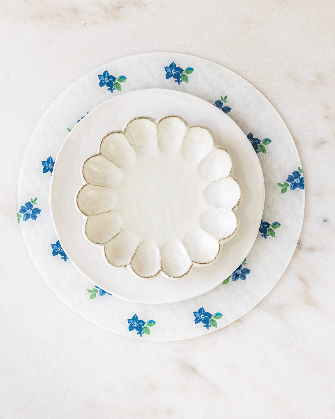 Round floral placemat in blues and whites at marble dining table.