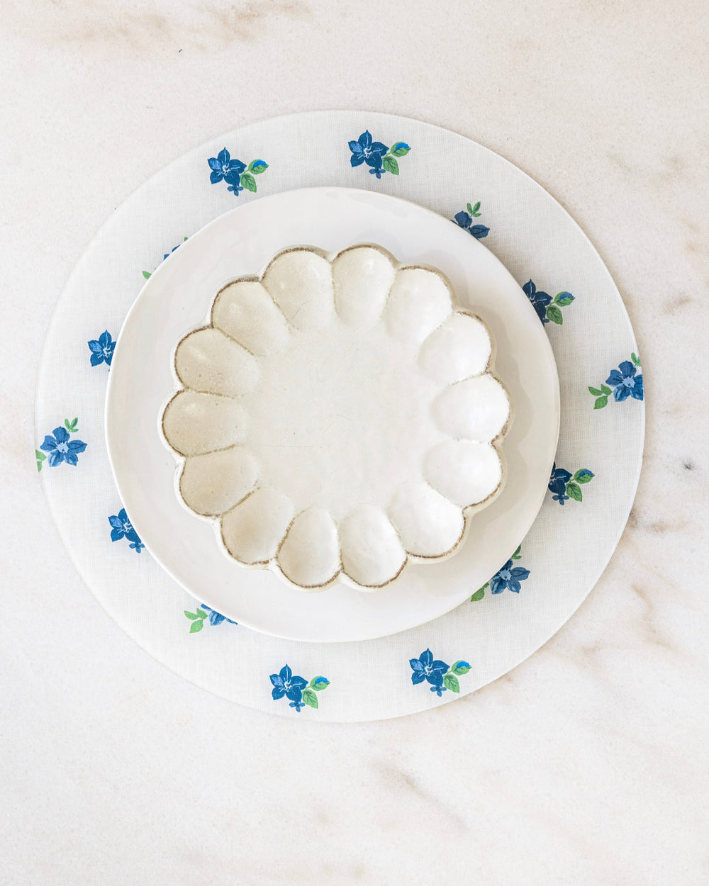 Round floral placemat in blues and whites at marble dining table.