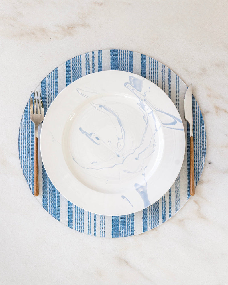 Round blue and white striped placemat with a white plate on a marble surface