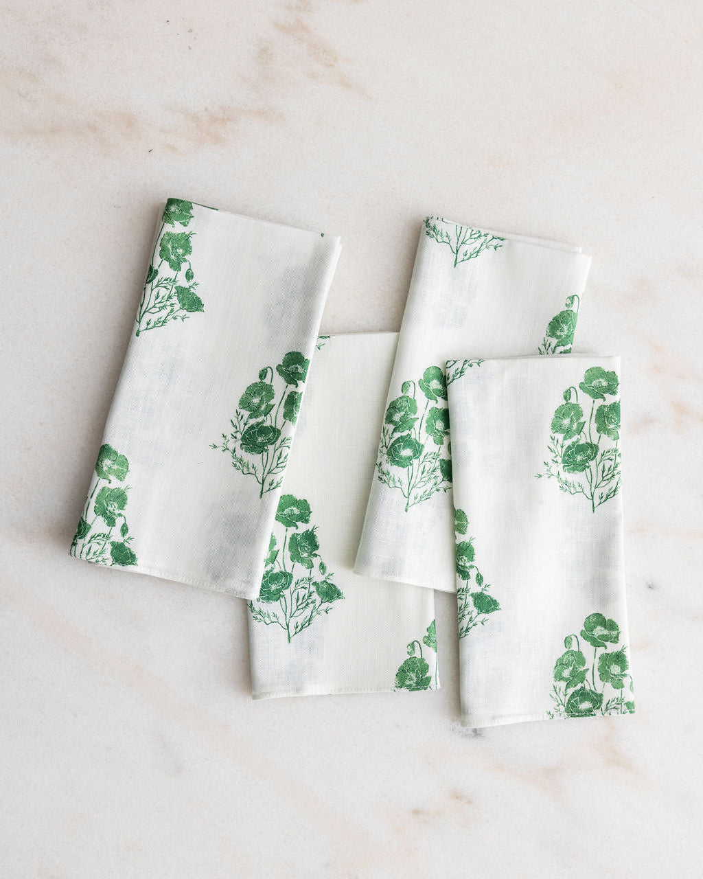 
                  
                    Set of four Poppy white napkins with green floral patterns on a light marble background
                  
                