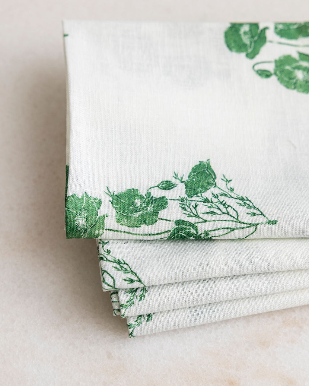 Stack of folded Proper Table white napkins with green floral patterns on a marble table