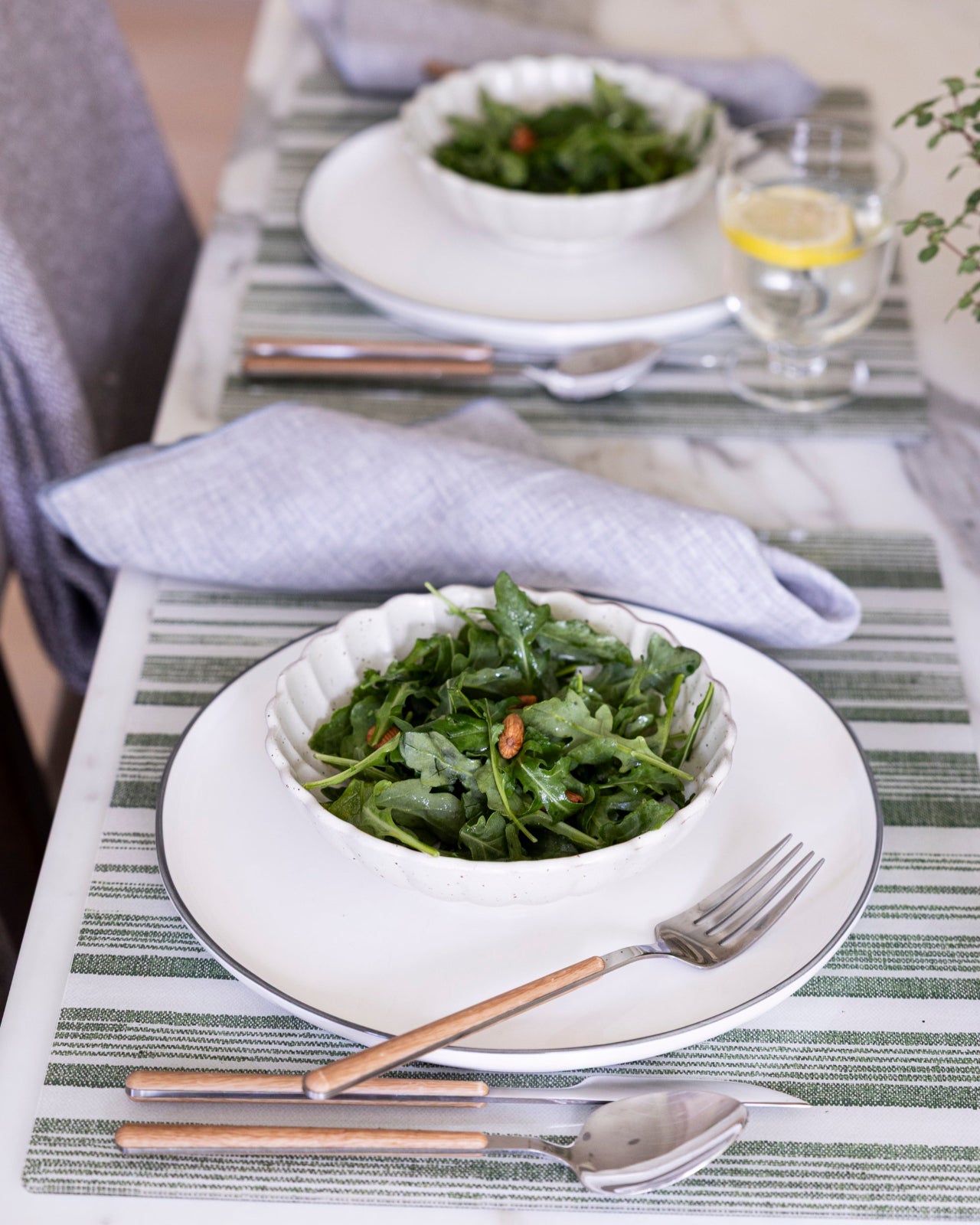 
                  
                    Two bowls of green salad on a table with green striped Proper Table placemats and cutlery.
                  
                