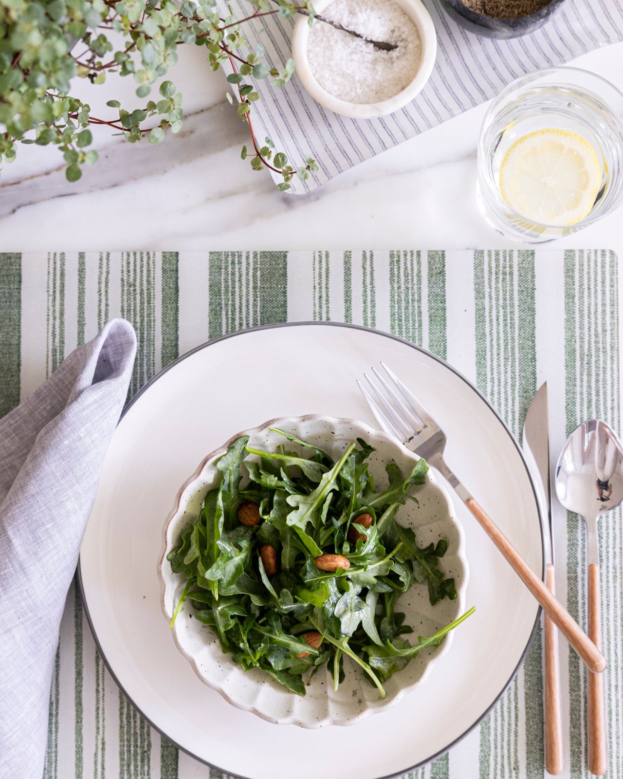 A collaboration between Proper Table and Nathan Turner Interors, a green and white stripe placemat  with a salad.