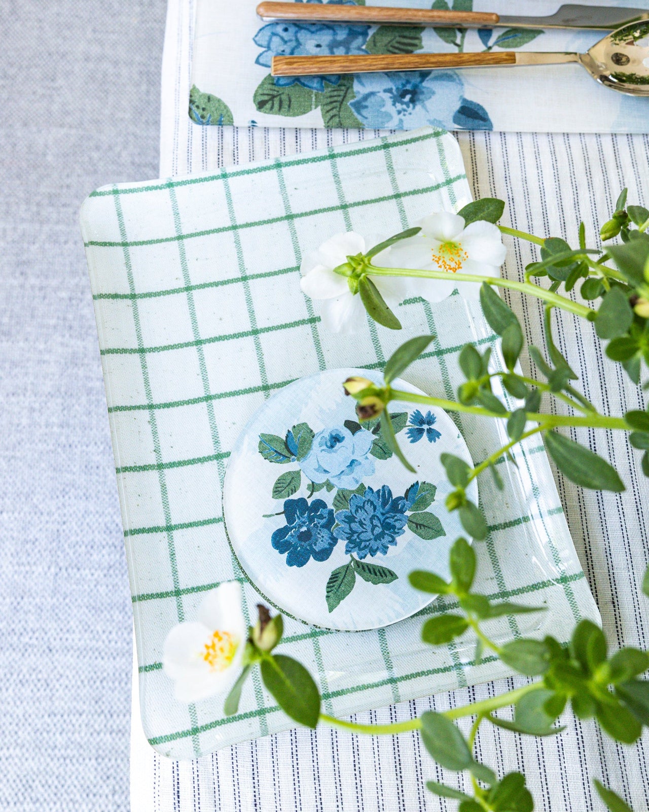 Table setting with Proper Table x Nathan Turner floral coasters and placemats, on a striped tablecloth.