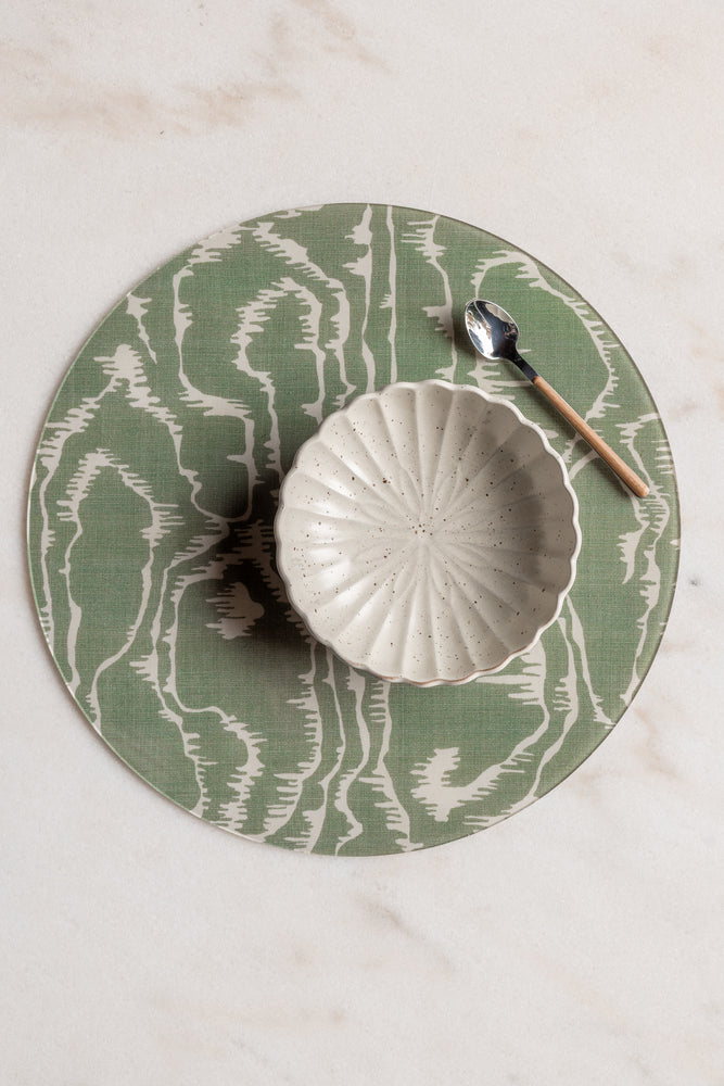 Round green and cream faux bois acrylic placemat from Proper Table x Leah O’Connell, styled with a scalloped ceramic bowl and wooden-handled spoon on marble.