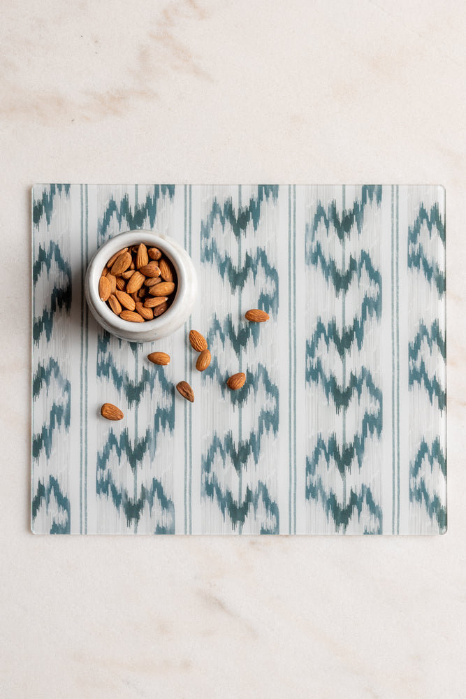 Rectangular blue and white ikat acrylic placemat from Proper Table x Leah O’Connell, styled on marble with almonds in a small white bowl. Placemat fabric is Isla from Leah O'Connell Textiles.