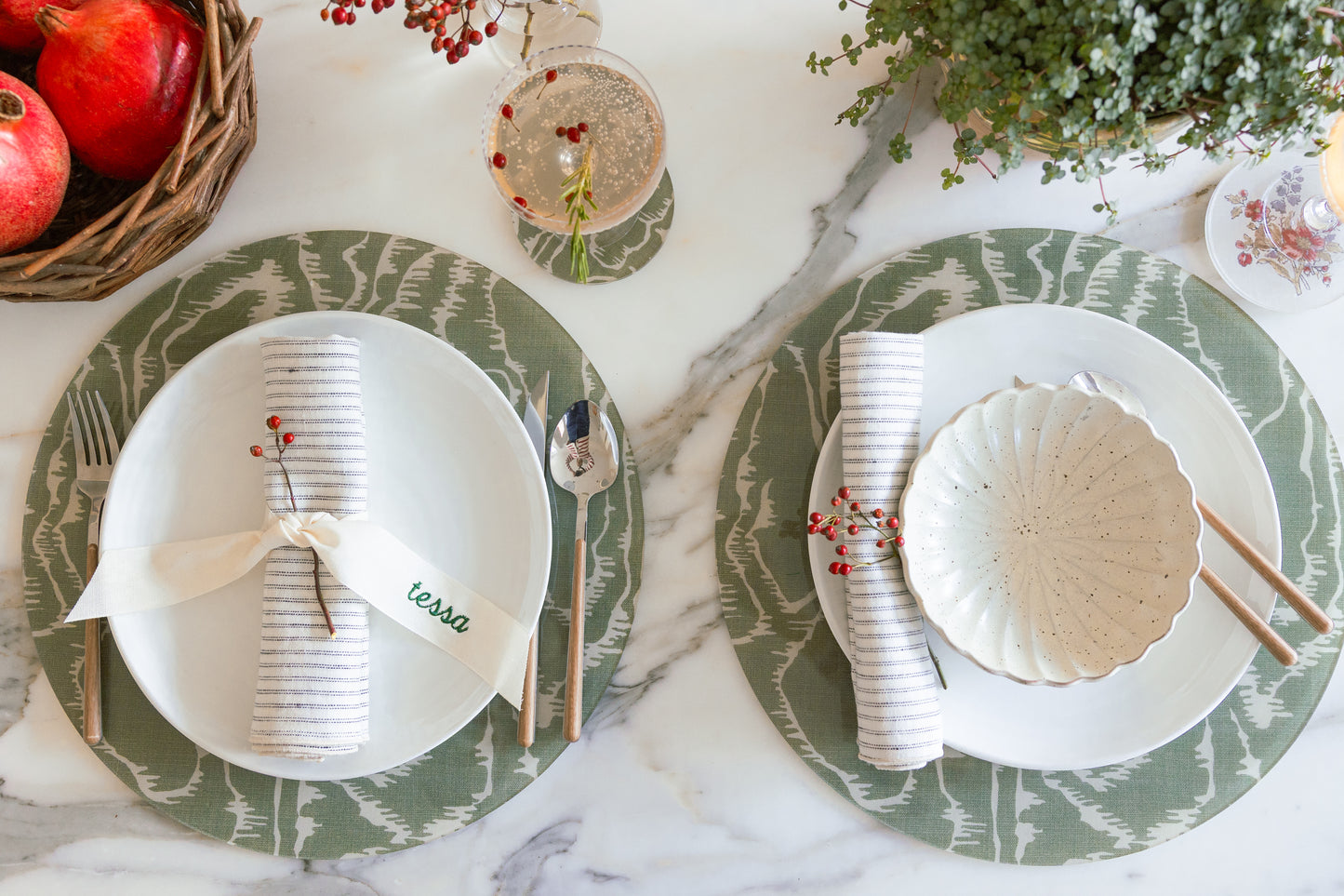 Two round green faux bois acrylic placemats from Proper Table x Leah O’Connell set with white plates, Eliot ticking napkins, and citrus cocktails on marble table. Placemat fabric is Tilda from Leah O'Connell Textiles.