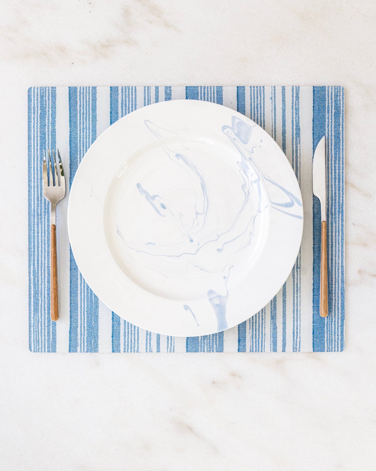 Rectangle placemat in blue striped fabric from a collaboration between Proper Table and Nathan Turner Interiors on marble.