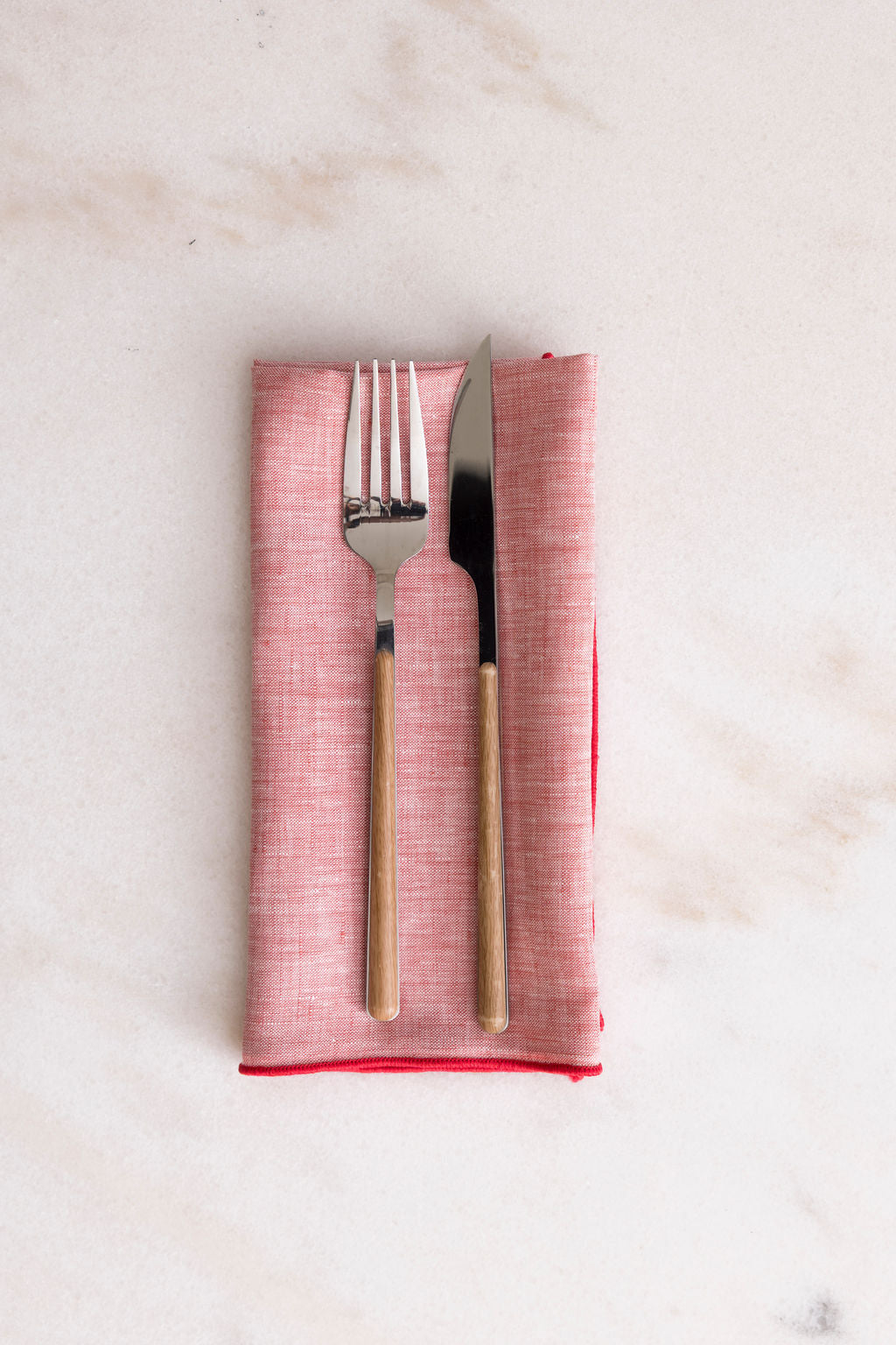Waller red chambray linen napkin set folded on marble with wood-handled fork and knife, red serged edge, set of four 18 inch cloth napkins