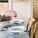 Proper Table classic, chic Campbell blue chambray acrylic placemats set with the cheerful blue gingham linen Mack napkins. The table is set for a celebratory dinner at home with candles and flowers.