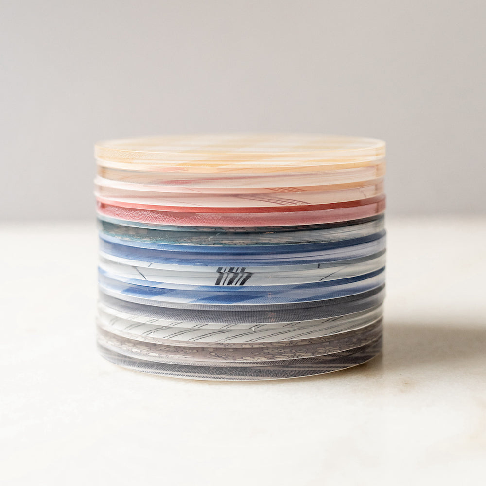 A stack of Proper Table colorful and fun acrylic coasters on a white marble table.
