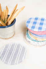 Stack of colorful linen-printed acrylic coasters on a marble table with hors d'oeuvres.